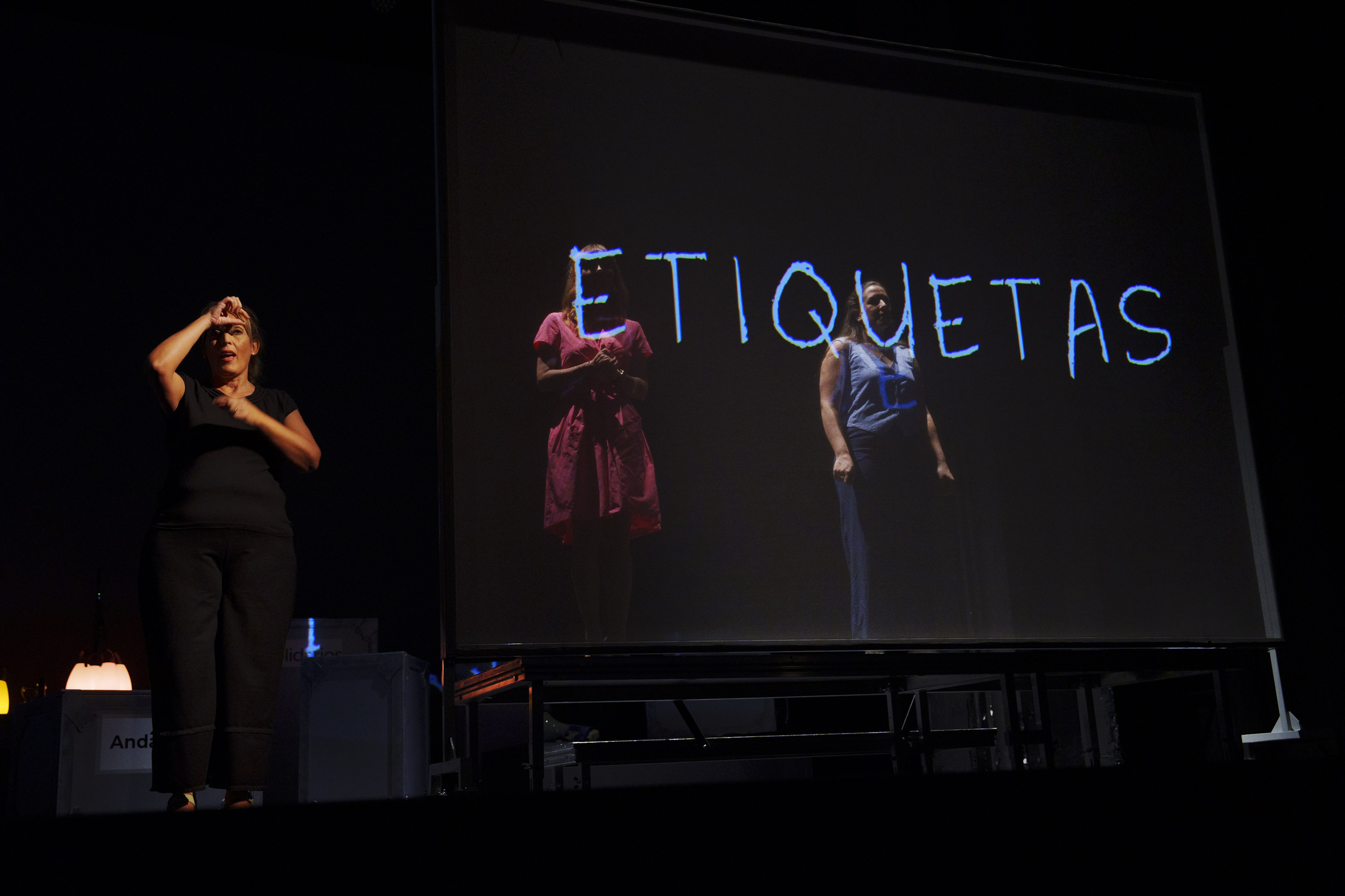 Las presentadoras en el escenario con la proyección de la palabra etiquetas sobre sus cuerpos