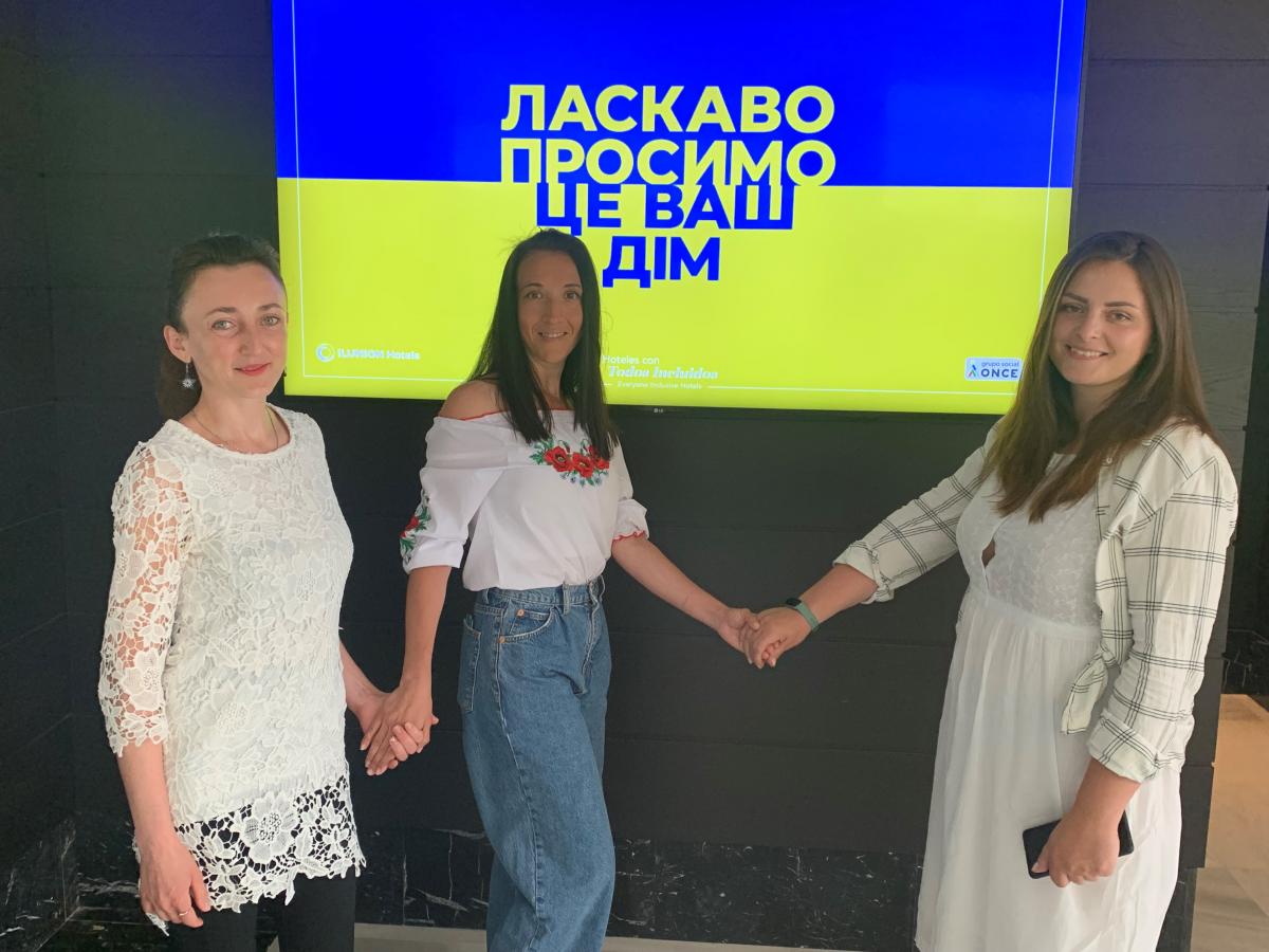 Tania, Amina y Victoria posan junto a la pantalla que proyecta la bandera ucraniana en el hall del hotel