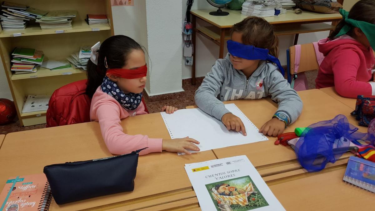 Dos alumnas con los ojos vendados trabajando conociendo la lectura en braille