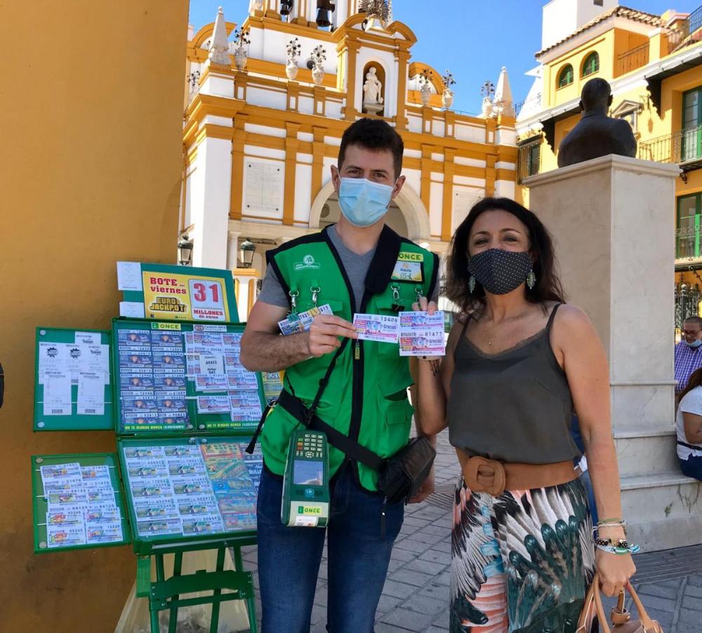 La presidenta del Parlamento de Andalucía, Marta Bosquet, compra el cupón a Alberto Ferrer en el Arco de la Macarena de Sevilla