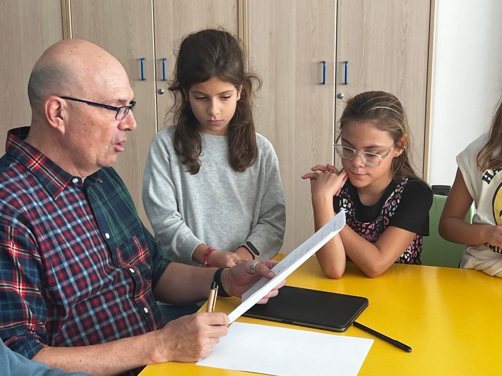 Dos alumnas con su profesor escuchando atentas su lectura