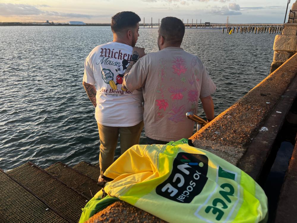 Los dos hermanos de espalda, mirando el mar, junto a su chaleco de vendedores