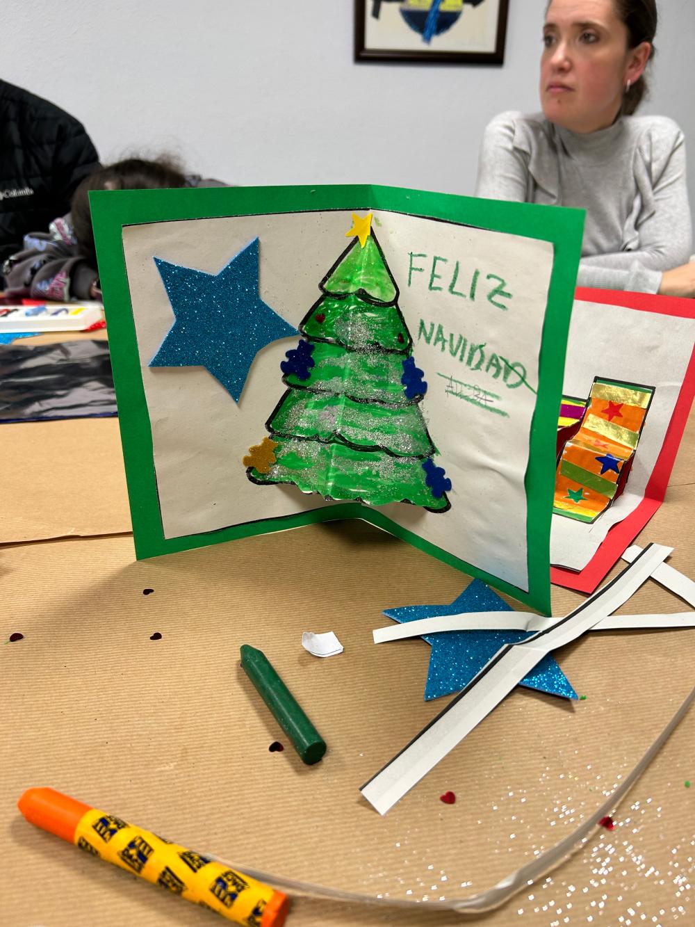 Tarjeta navideña elaborada por uno de los niños asistentes: árbol de navidad en tres dimensiones y estrella azul con brillantina