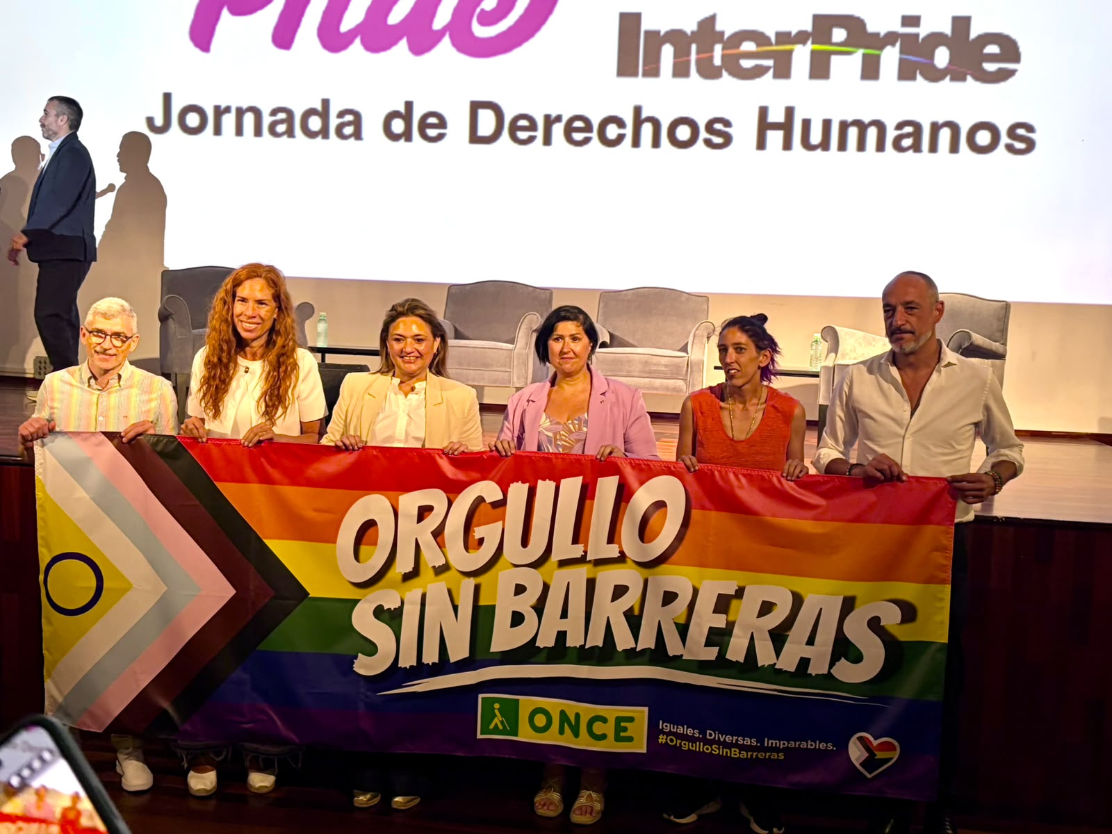 La directora de la ONCE en Torremolinos con la alcaldesa de la ciudad en la presentación del Orgullo tras la pancarta de la ONCE